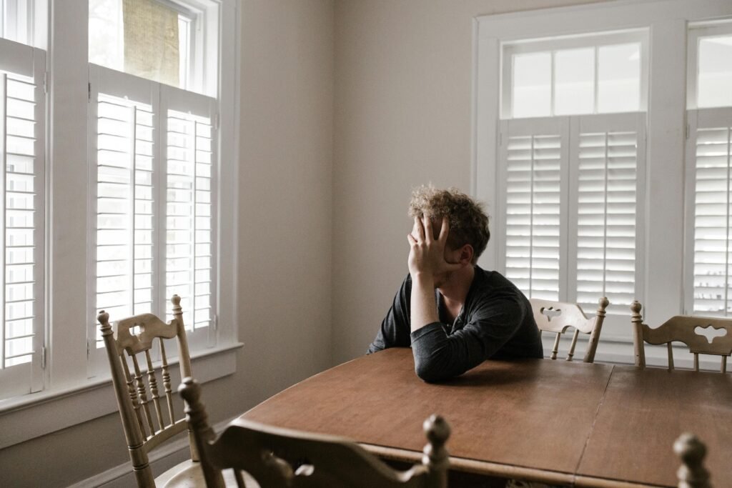 pexels-photo-3132388-3132388 A man sits alone at a table in a bright room, displaying deep contemplation.