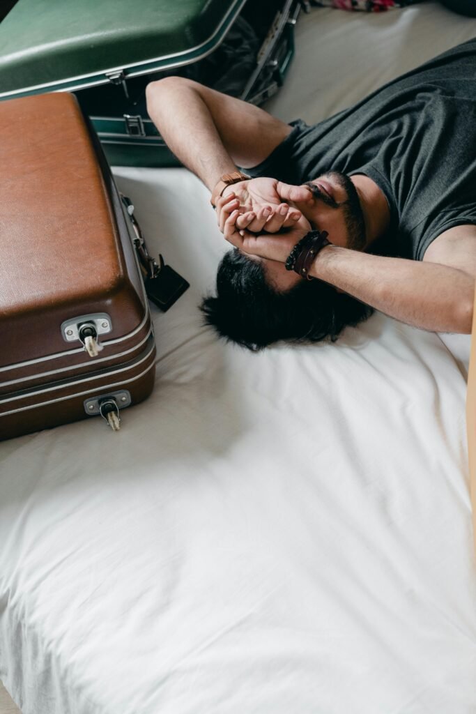 A young man rests on a bed, surrounded by luggage, reflecting a travel or moving theme.