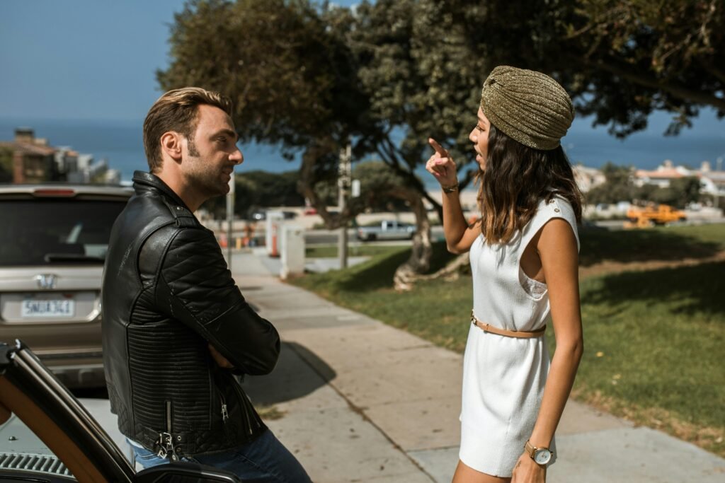 An interracial couple having an intense conversation near a park with an ocean view, expressing emotions vividly.